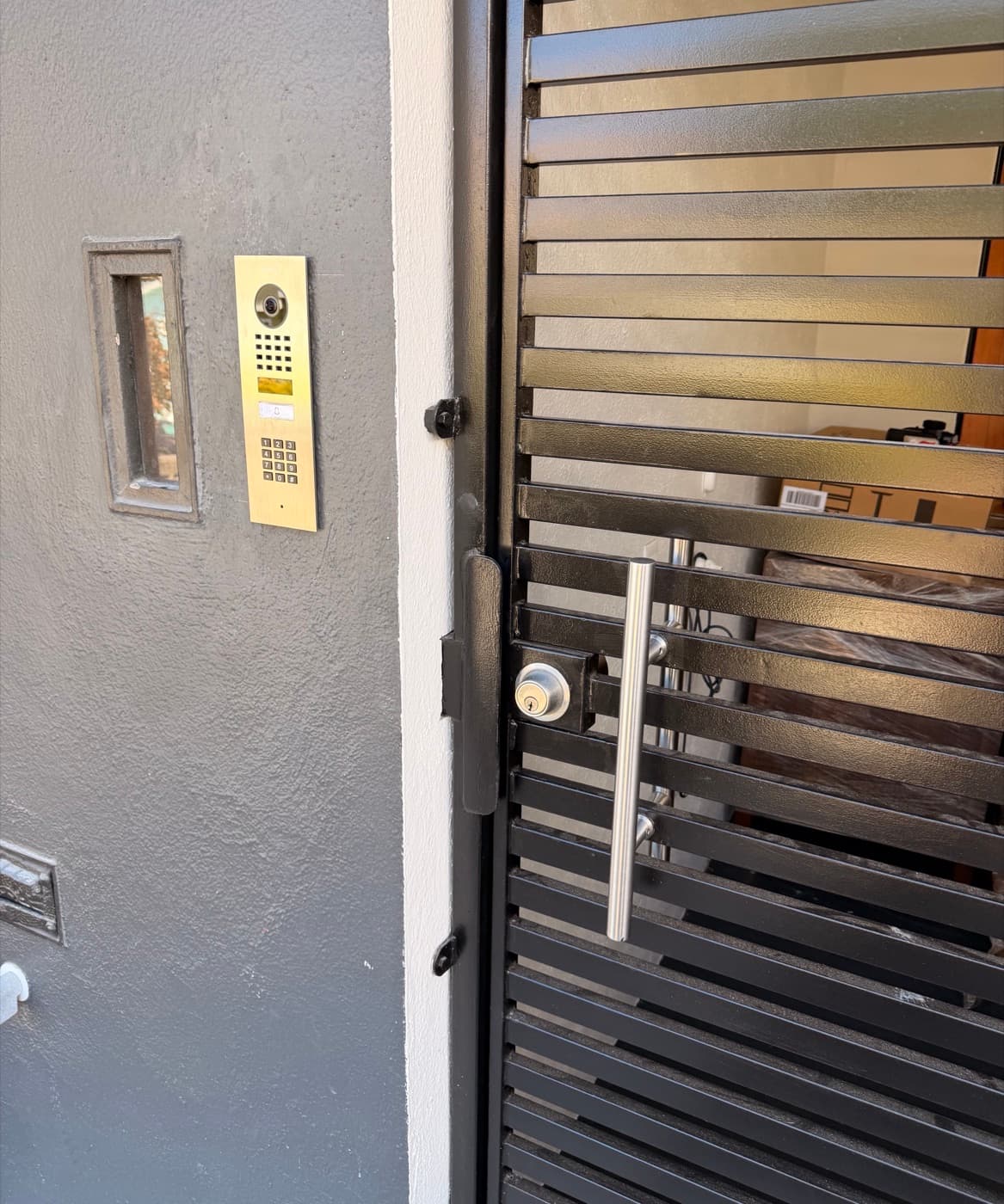 Flush-mounted video intercom with keypad beside a slatted entry gate